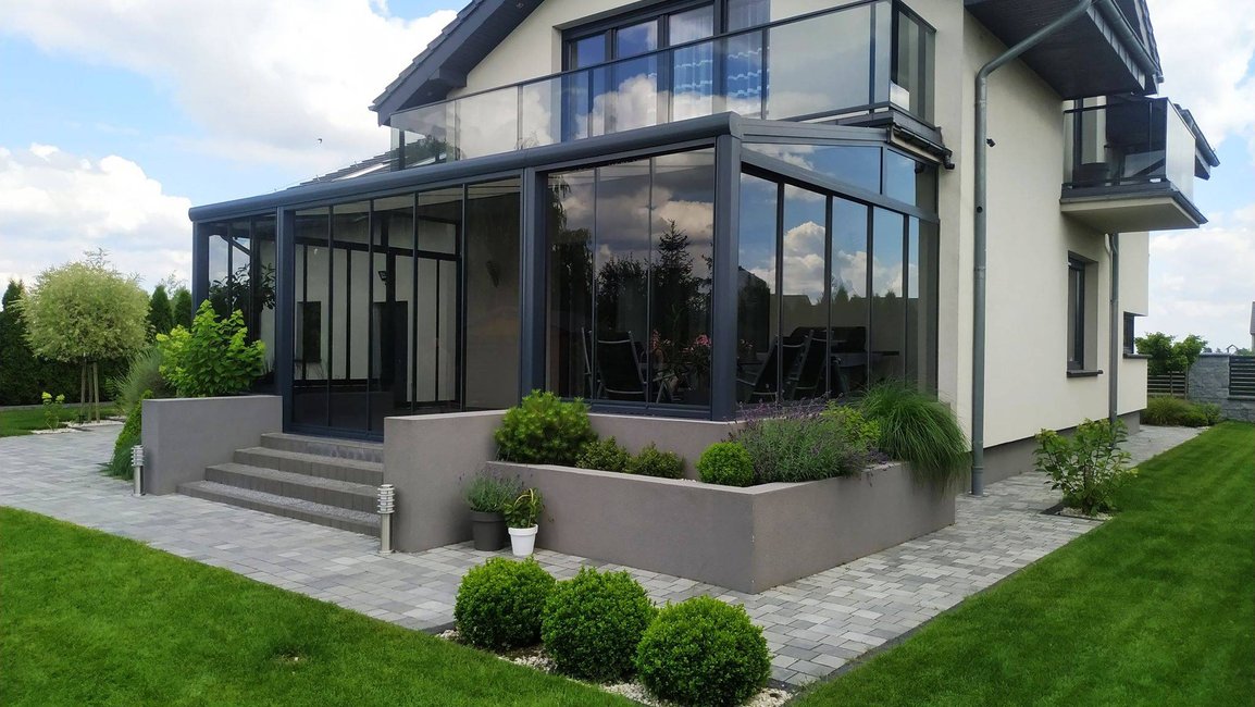 Moderní zimní zahrada z hliníkové konstrukce v antracitové barvě rozšiřuje obytný prostor domu a nabízí celoroční využití s maximálním prosvětlením a výhledem do zahrady.