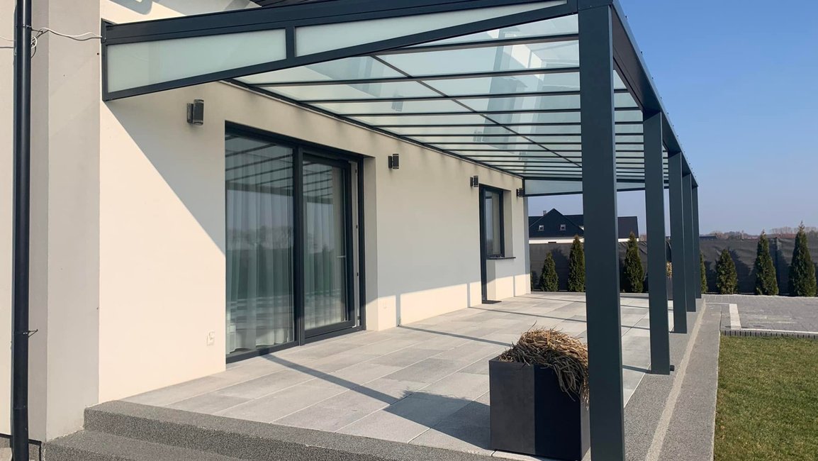 Moderní hliníková pergola s prosklenou střechou podél celé terasy rodinného domu, připravená na budoucí zasklení a stínění.
