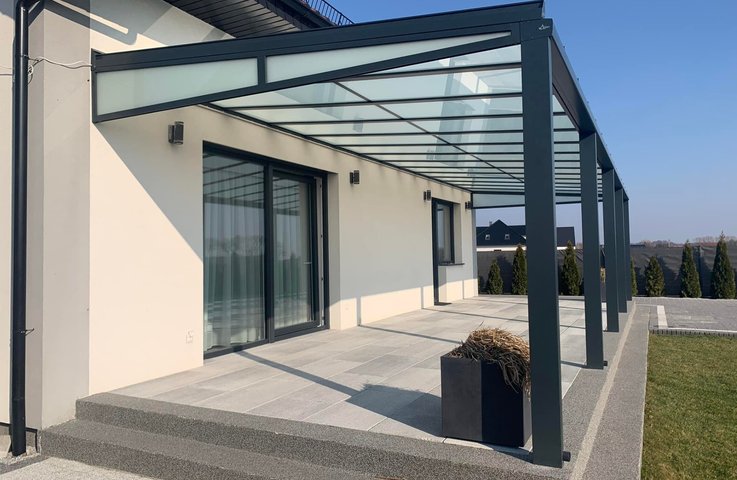 Moderní hliníková pergola s prosklenou střechou podél celé terasy rodinného domu, připravená na budoucí zasklení a stínění.
