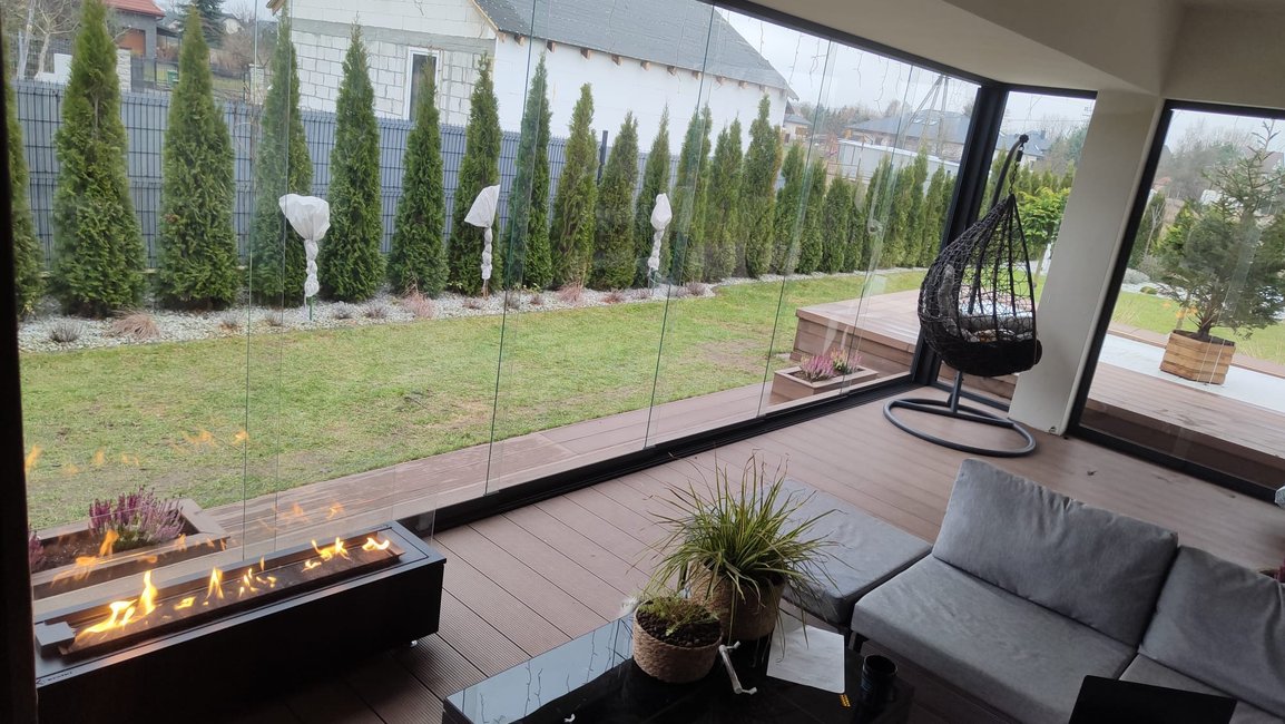 Zasklená terasa s bezrámovým zasklením a biokrbem vytváří útulný celoroční obývák na zahradě