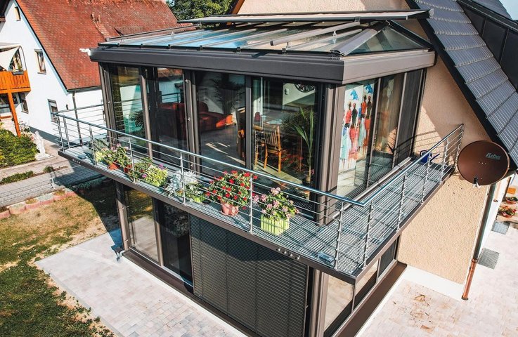 Patrová zimní zahrada Hezký stín s prosklenou střechou a velkými posuvnými okny na rodinném domě, přechod na balkon s květinami.