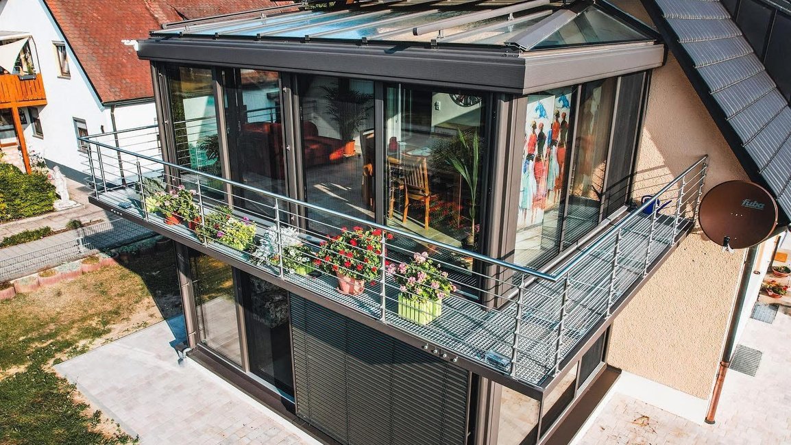 Patrová zimní zahrada Hezký stín s prosklenou střechou a velkými posuvnými okny na rodinném domě, přechod na balkon s květinami.