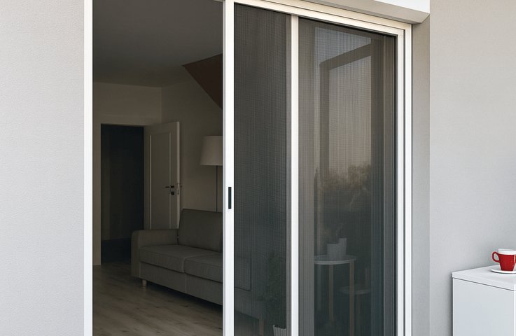Moderní posuvná síť proti hmyzu v bílém hliníkovém rámu chrání terasové dveře do obývacího pokoje a umožňuje pohodlné větrání bez komárů a much