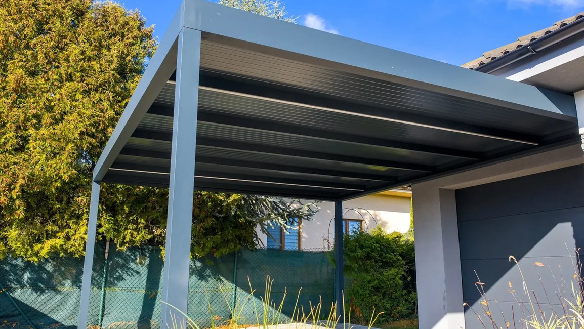 Moderní hliníkový carport v antracitovém provedení spolehlivě ochrání váš vůz před krupobitím, UV zářením i nánosy sněhu. Díky integrovanému svodu dešťové vody vnitřkem sloupů a skrytému kotvení pod dlažbou působí celá stavba absolutně čistým a minimalistickým dojmem. Pokud při zemních pracích a přípravě betonových patek myslíte i na přivedení silového kabelu, stane se masivní hliníkový sloup ideálním místem pro instalaci domácí nabíjecí stanice (wallboxu) pro váš elektromobil.