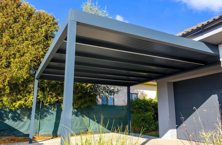 Moderní hliníkový carport v antracitovém provedení spolehlivě ochrání váš vůz před krupobitím, UV zářením i nánosy sněhu. Díky integrovanému svodu dešťové vody vnitřkem sloupů a skrytému kotvení pod dlažbou působí celá stavba absolutně čistým a minimalistickým dojmem. Pokud při zemních pracích a přípravě betonových patek myslíte i na přivedení silového kabelu, stane se masivní hliníkový sloup ideálním místem pro instalaci domácí nabíjecí stanice (wallboxu) pro váš elektromobil.