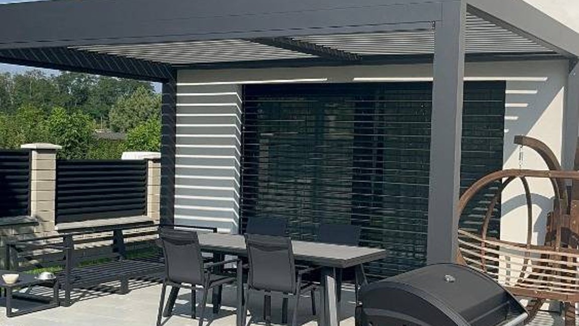„Bioklimatická hliníková pergola s lamelovou střechou na terase moderního domu, venkovní žaluzie, zahradní posezení a gril.“