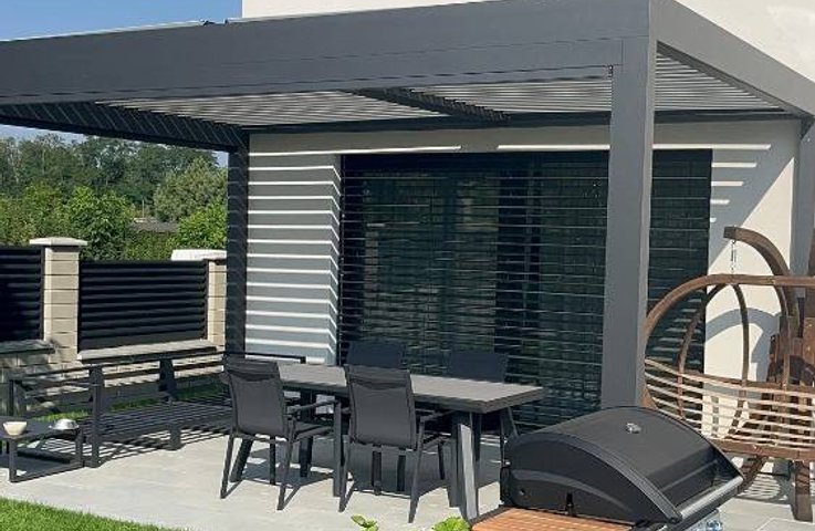 „Bioklimatická hliníková pergola s lamelovou střechou na terase moderního domu, venkovní žaluzie, zahradní posezení a gril.“