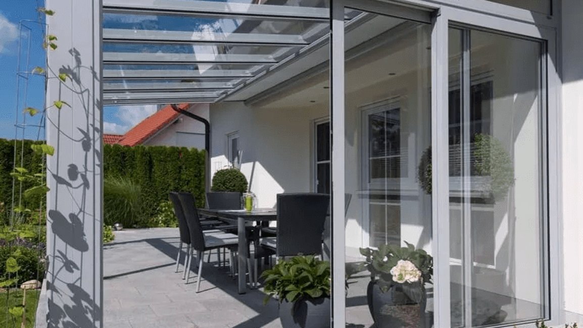 Moderní terasa u rodinného domu je chráněná rámovým hliníkovým zasklením s prosklenou střechou. Vzniká tak elegantní kryté posezení, které lze využívat od jara do podzimu a navazuje přímo na zahradu.