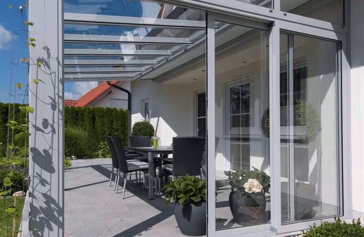 Moderní terasa u rodinného domu je chráněná rámovým hliníkovým zasklením s prosklenou střechou. Vzniká tak elegantní kryté posezení, které lze využívat od jara do podzimu a navazuje přímo na zahradu.