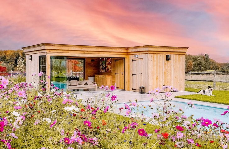 Bezrámově zasklený dřevěný zahradní pavilon u bazénu, který rozšiřuje terasu a chrání posezení před počasím.