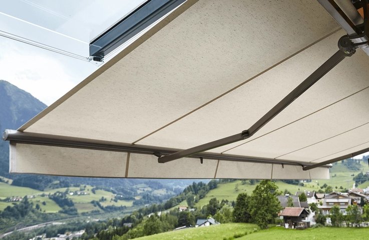 Moderní výsuvná markýza s horním krytem zastíní terasu rodinného domu a chrání látku před deštěm i nečistotami. Díky velkému výsuvu vzniká pohodlné místo pro venkovní stolování s krásným výhledem do okolní krajiny