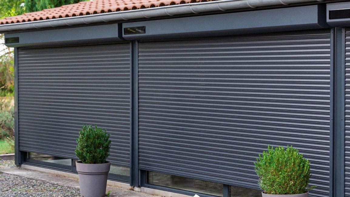 Venkovní rolety s motorem na solární pohon v antracitové barvě, stažené před velkými okny rodinného domu.