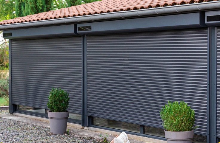 Venkovní rolety s motorem na solární pohon v antracitové barvě, stažené před velkými okny rodinného domu.