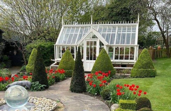 Viktorianský skleník na zahradě s květinami