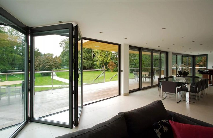 Skládací prosklený systém mezi obývacím pokojem a terasou – velkoformátové hliníkové dveře otevřené do zahrady, které spojují interiér s exteriérem a rozšiřují obytný prostor.